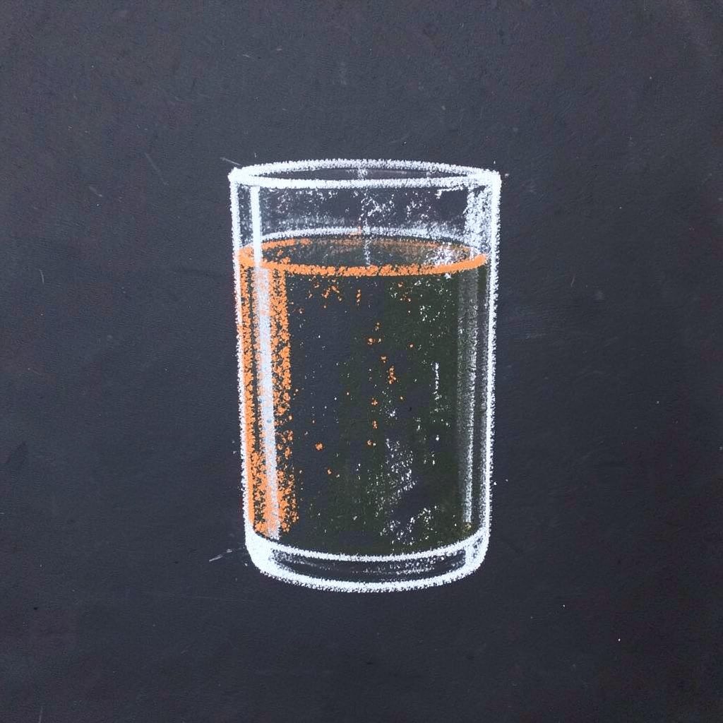Soft chalk sketch of wheatgrass sprigs and a juice glass on a dark slate board, warm beige and green tones